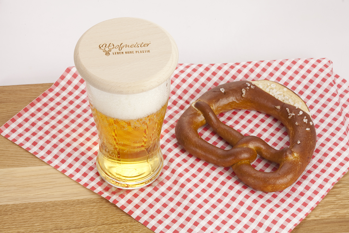Glas mit Bier und Bierglasdeckel aus Holz und Brezel