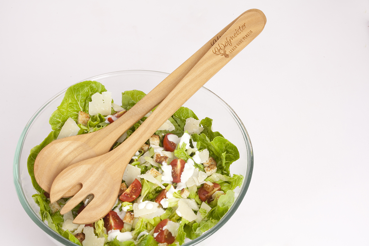 Geöltes Salatbesteck aus Kirschholz liegt auf einer Glasschale mit Salat