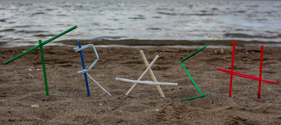Strohhalme aus Plastik am Strand als Wort TRASH geformt